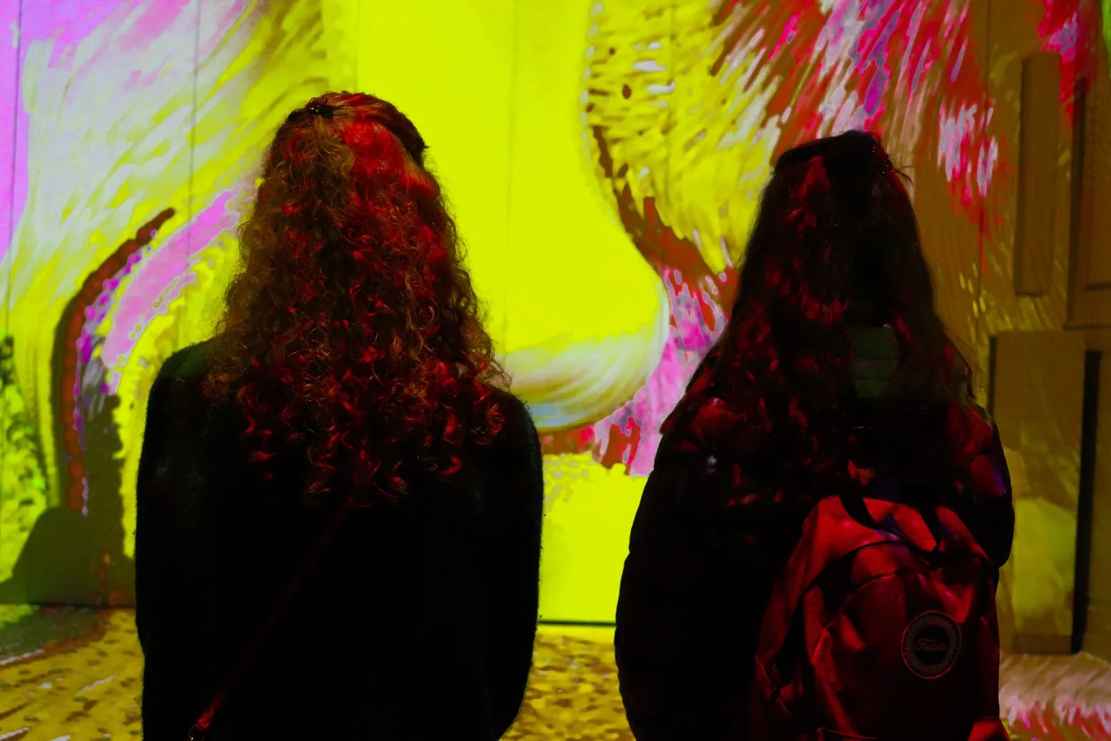 Deux visiteuses de dos face à des projections colorées couvrant les murs et le sol d'une salle d'art immersif
