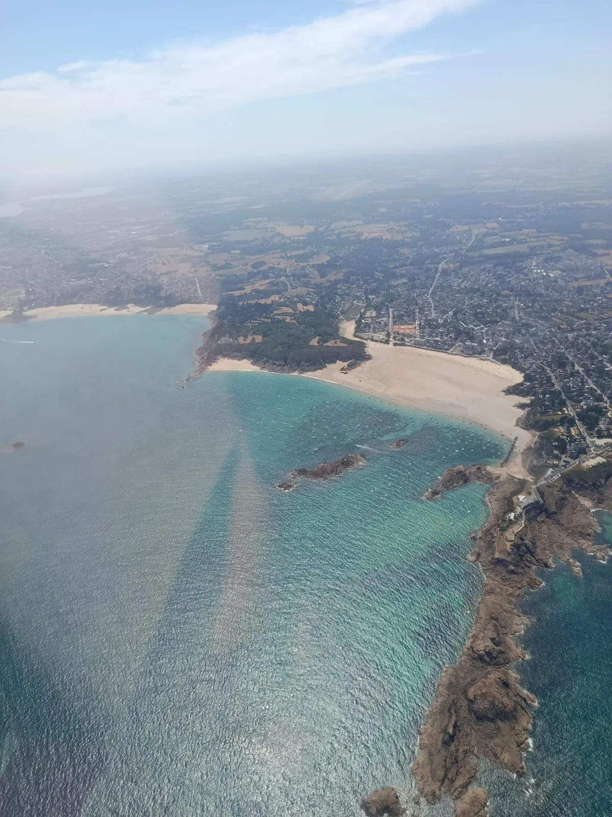 Plage et pointe rocheuse de la Côte d'Émeraude aux eaux turquoise, vues du ciel en ULM