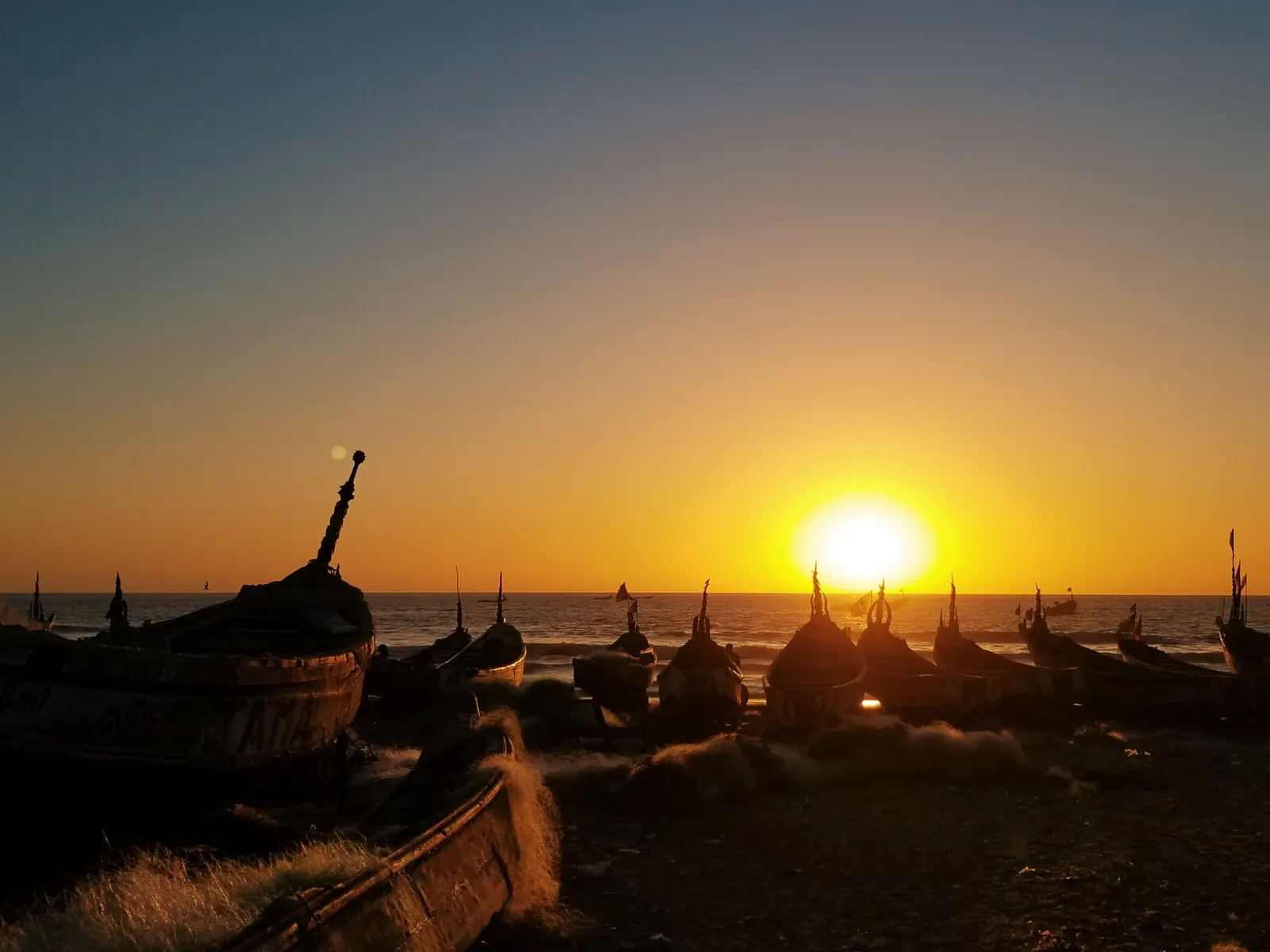 Silhouettes de pirogues de pêcheurs sur la plage de Cap Skirring au coucher du soleil