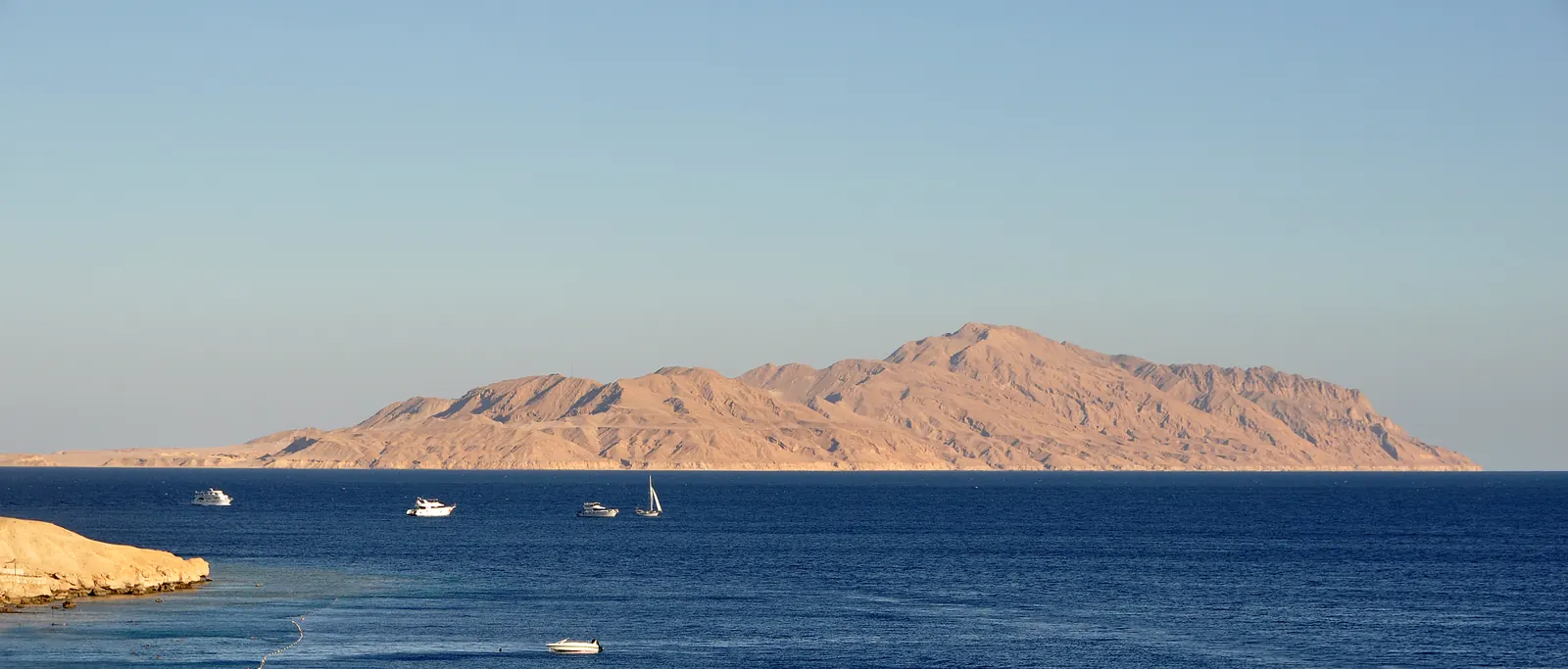 L'île de Tiran vue depuis la côte égyptienne, avec des bateaux de plongée mouillés dans le détroit