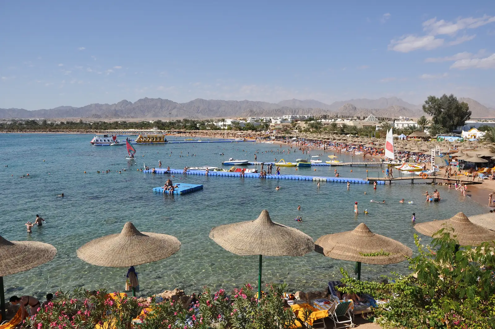 La plage de Naama Bay à Charm el-Cheikh, ses parasols de paille, son ponton et les montagnes du Sinaï au fond