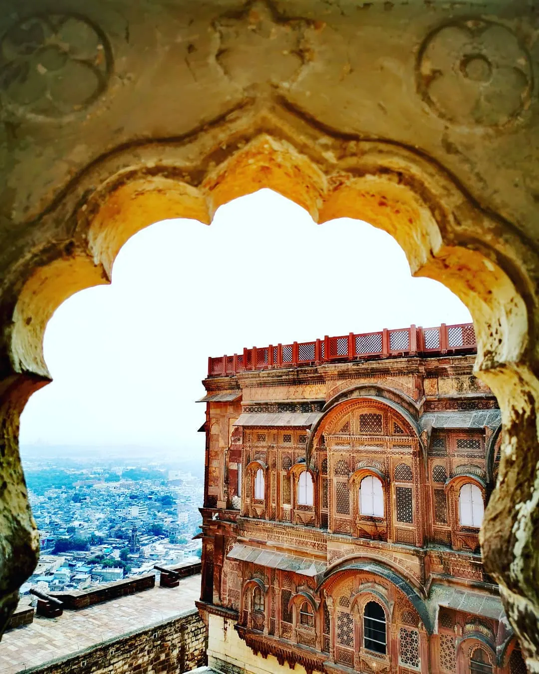 Façade sculptée du fort de Mehrangarh vue à travers une arche polylobée, avec les maisons bleues de Jodhpur en contrebas