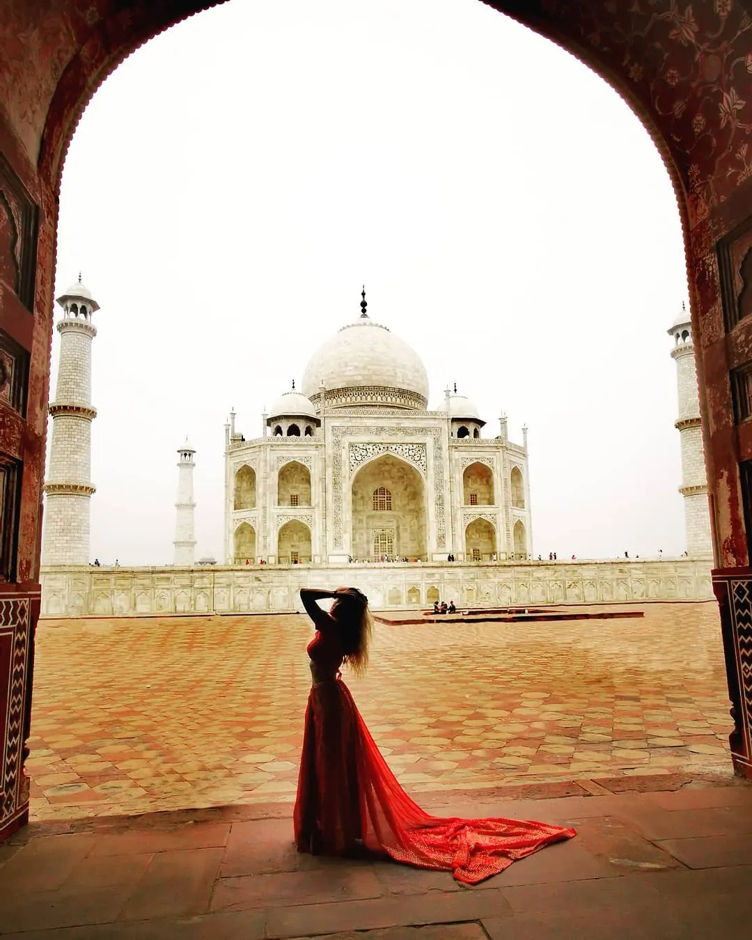Le Taj Mahal d'Agra vu depuis une arche de grès rouge, avec ses quatre minarets et son dôme de marbre blanc dans la brume