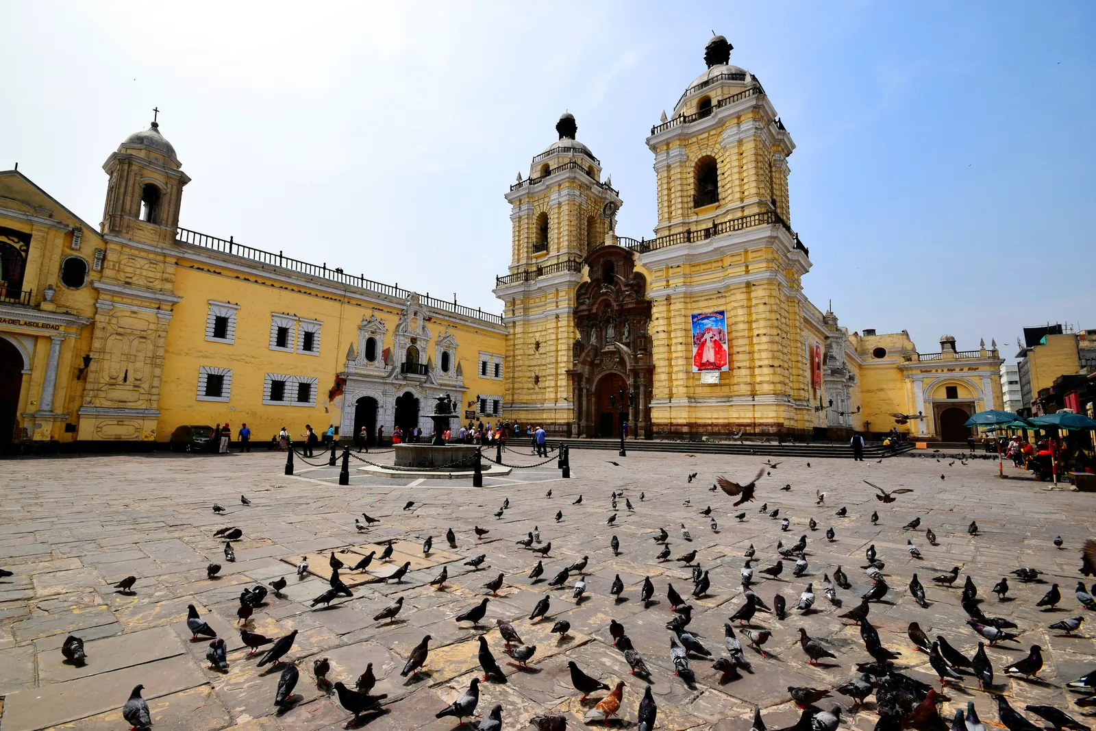 La basilique et le couvent de San Francisco de Lima, façade jaune à deux tours, sur une place couverte de pigeons
