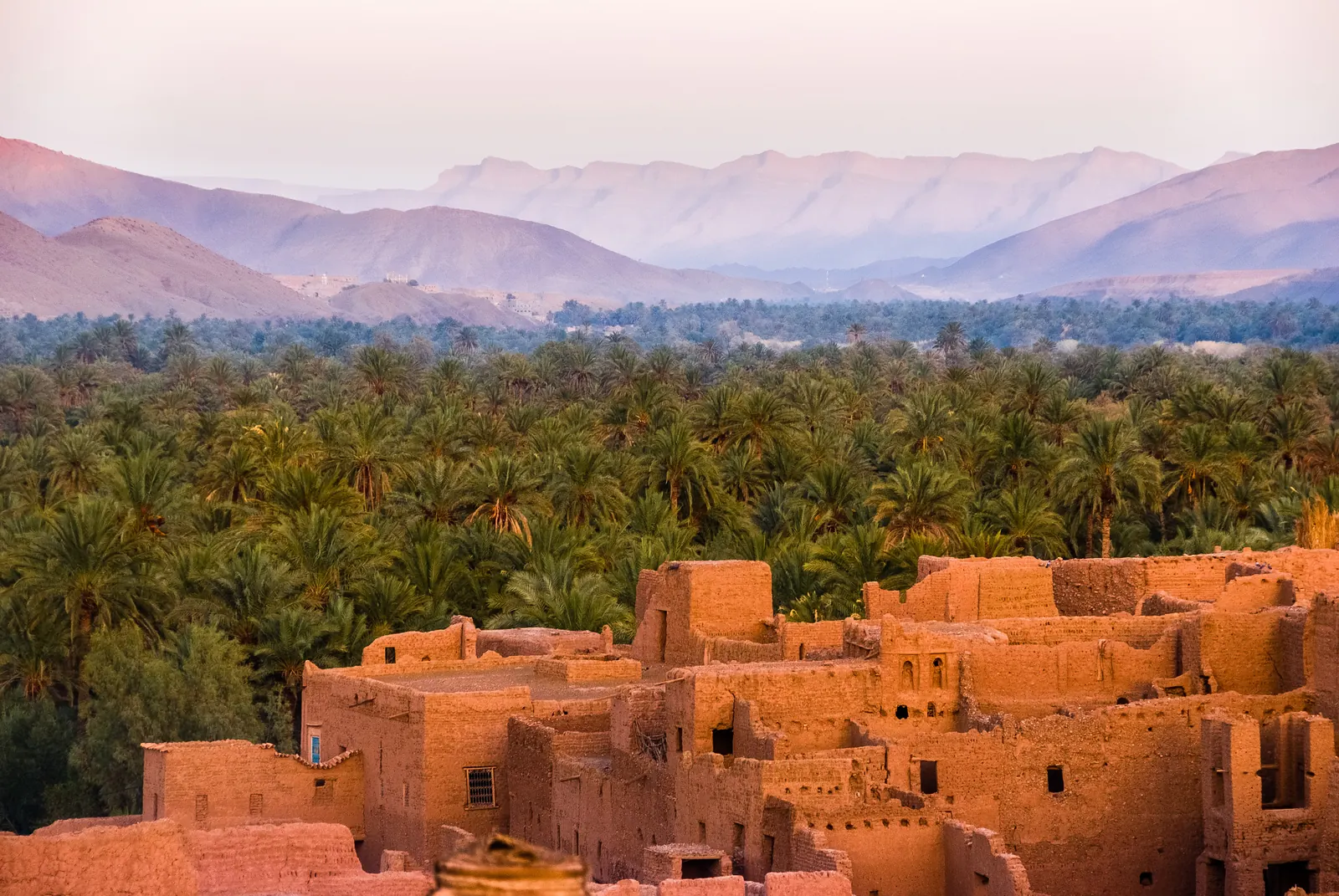 Un ksar ocre au premier plan devant la palmeraie et les montagnes de la vallée du Drâa