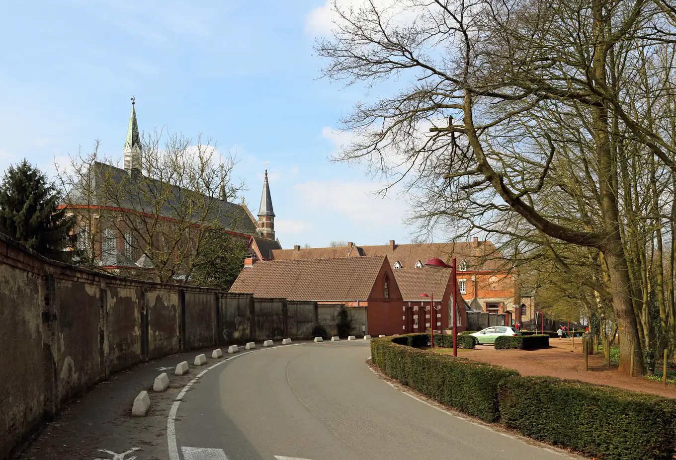 Route qui longe le mur d'enceinte de l'abbaye du Mont des Cats, avec l'église néogothique et ses flèches en arrière-plan