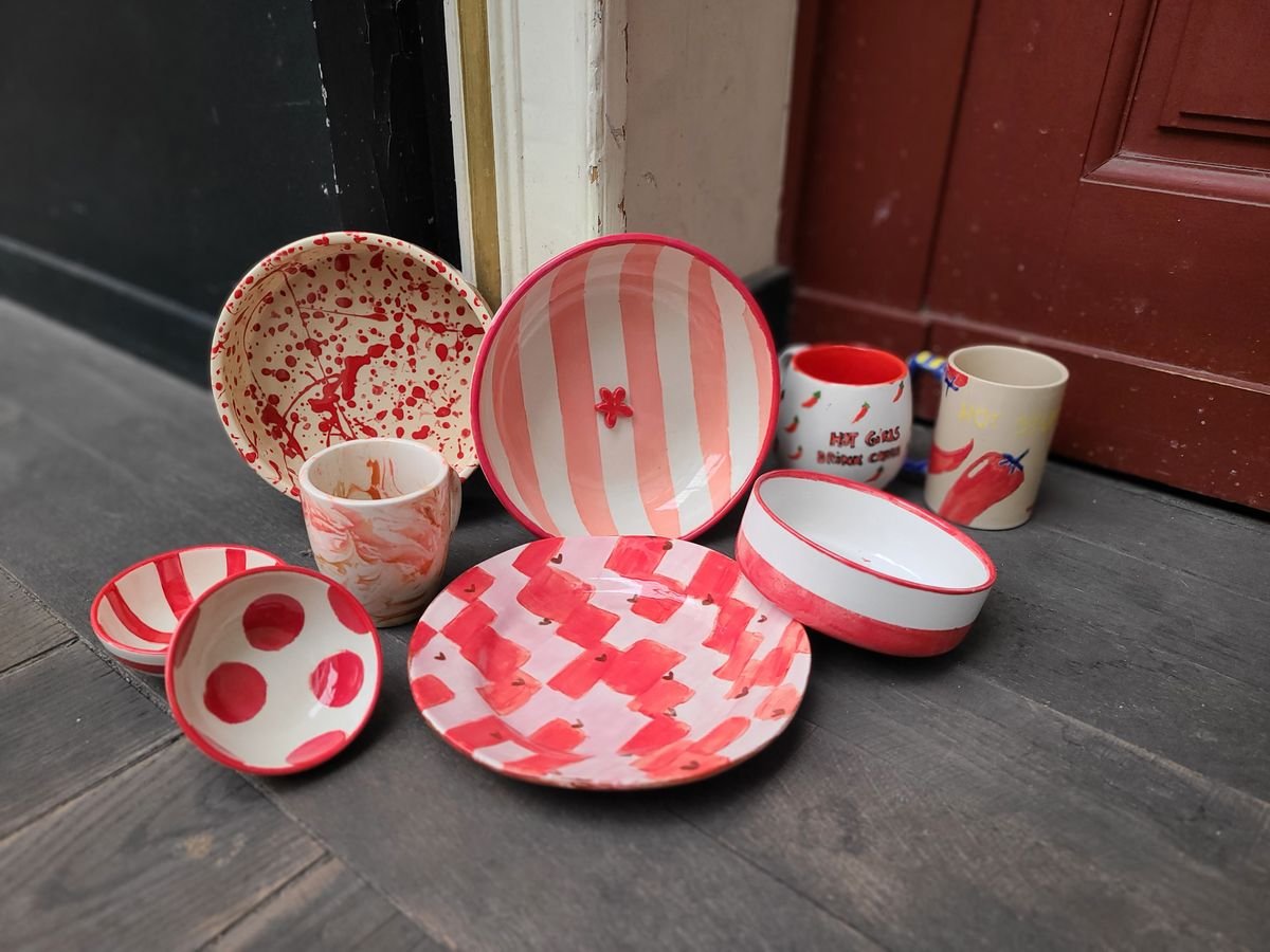 Bols, assiettes et tasses peints à pois, à rayures et à damier rouges et roses, posés sur le sol du Passage Pommeraye