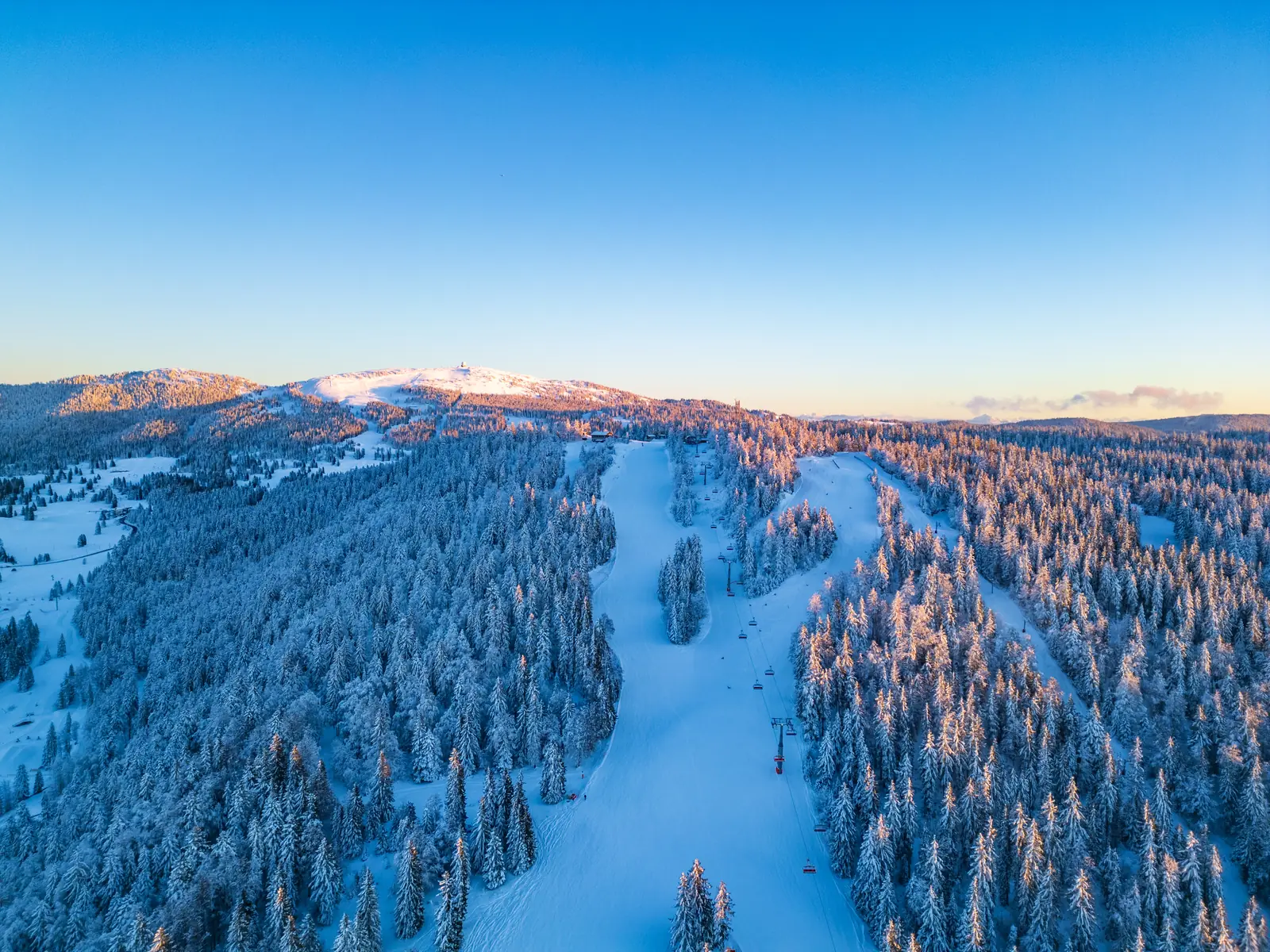 Vue aérienne des pistes au milieu des forêts enneigées, avec la Dôle et son radome au loin