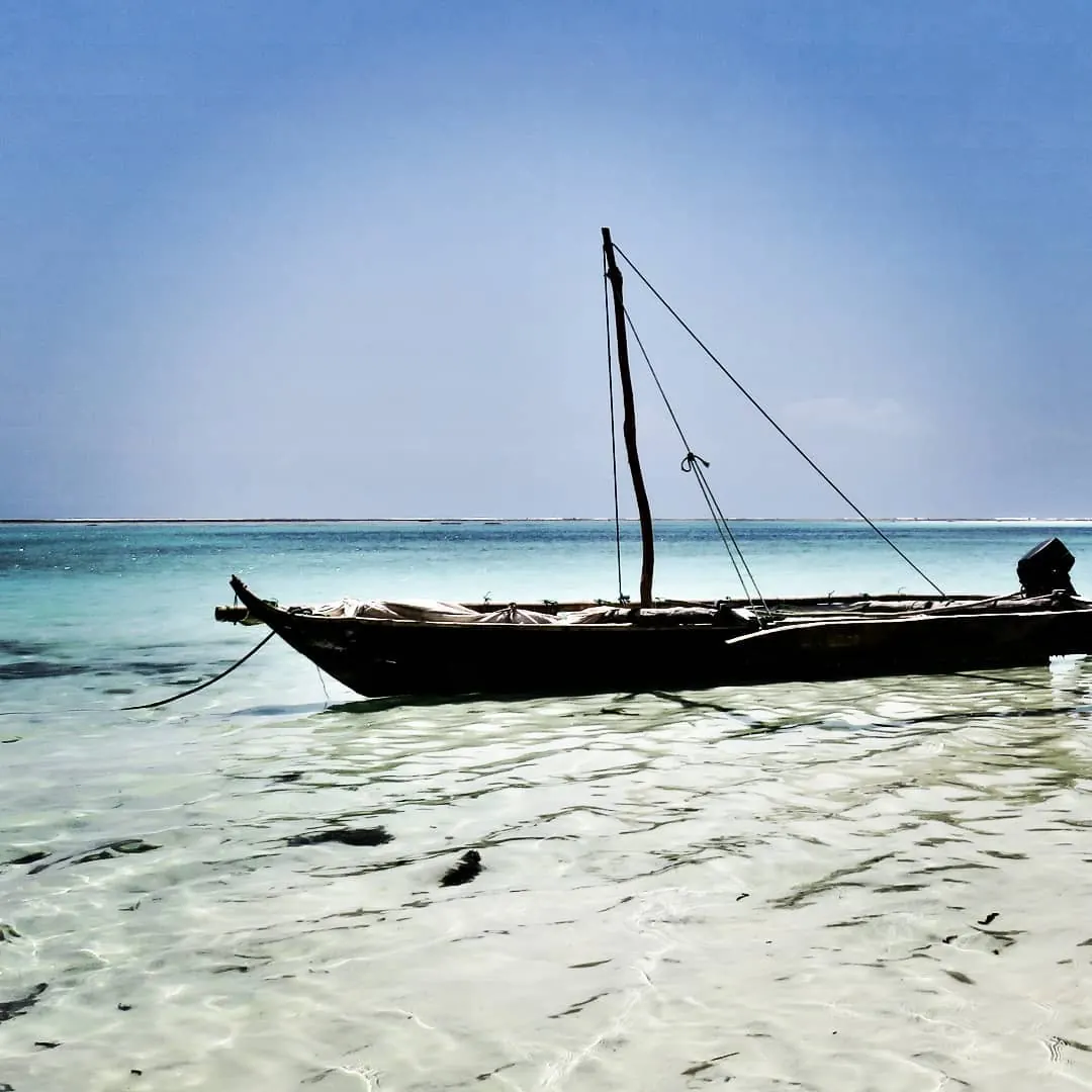 Pirogue à voile traditionnelle en bois, mât nu, mouillée dans l'eau claire d'un lagon de Zanzibar