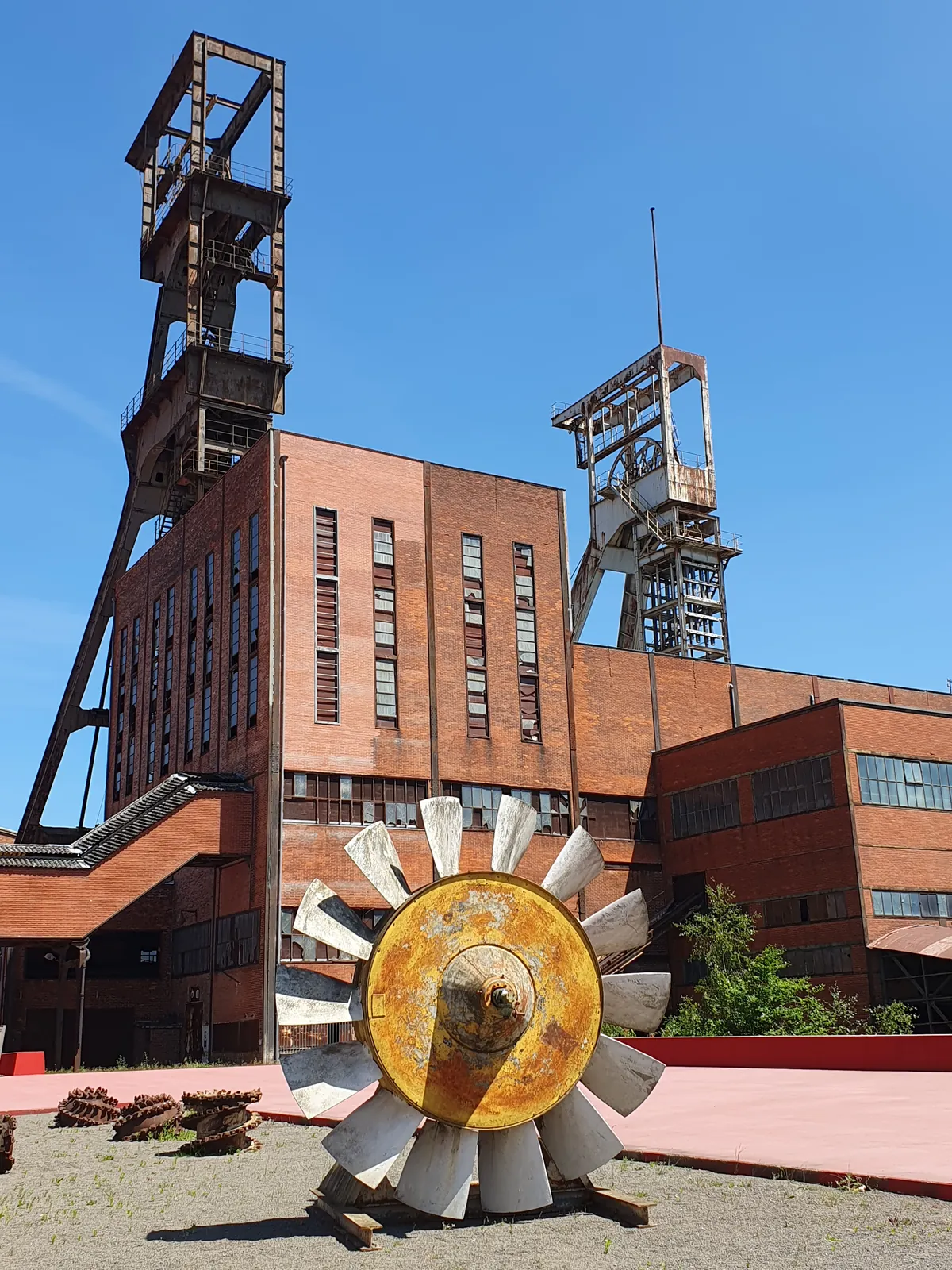 Deux chevalements et un bâtiment en brique du carreau Wendel, une roue de ventilateur au premier plan